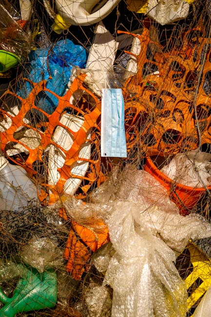 A person's hand wearing a pink rubber glove is holding a large, transparent plastic bag filled with numerous clear plastic bottles and containers, some with visible caps and ridges. The background features a plain yellow curtain or fabric, providing a neutral backdrop that highlights the focus on the waste items. The scene is well-lit, emphasizing the reflective surfaces of the plastic bottles and the crinkled texture of the bag. This image illustrates the handling of recyclable plastic waste, potentially as part of a rubbish removal or recycling process supported by independent waste collection services. The arrangement emphasizes the importance of proper waste segregation and the preparedness for collection or disposal of plastic materials in a domestic or commercial context, aligning with the broader topic of rubbish clearance and alternative waste handling solutions.